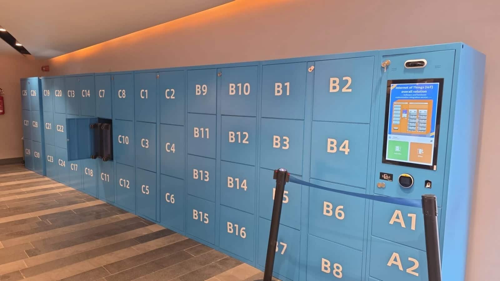 The wall of blue luggage lockers with the touch-screen kiosk inside the Molo Beverello terminal, Naples